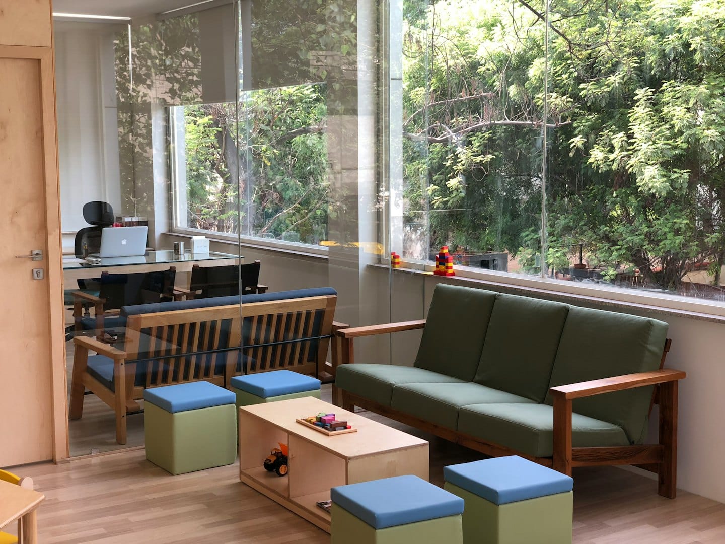 Modern office lounge with light wood furniture and green cushions.